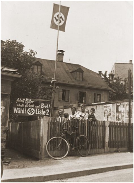 Young Nazi party supporters stand next to an election poster that reads -Adolf Hitler will provide work and bread!